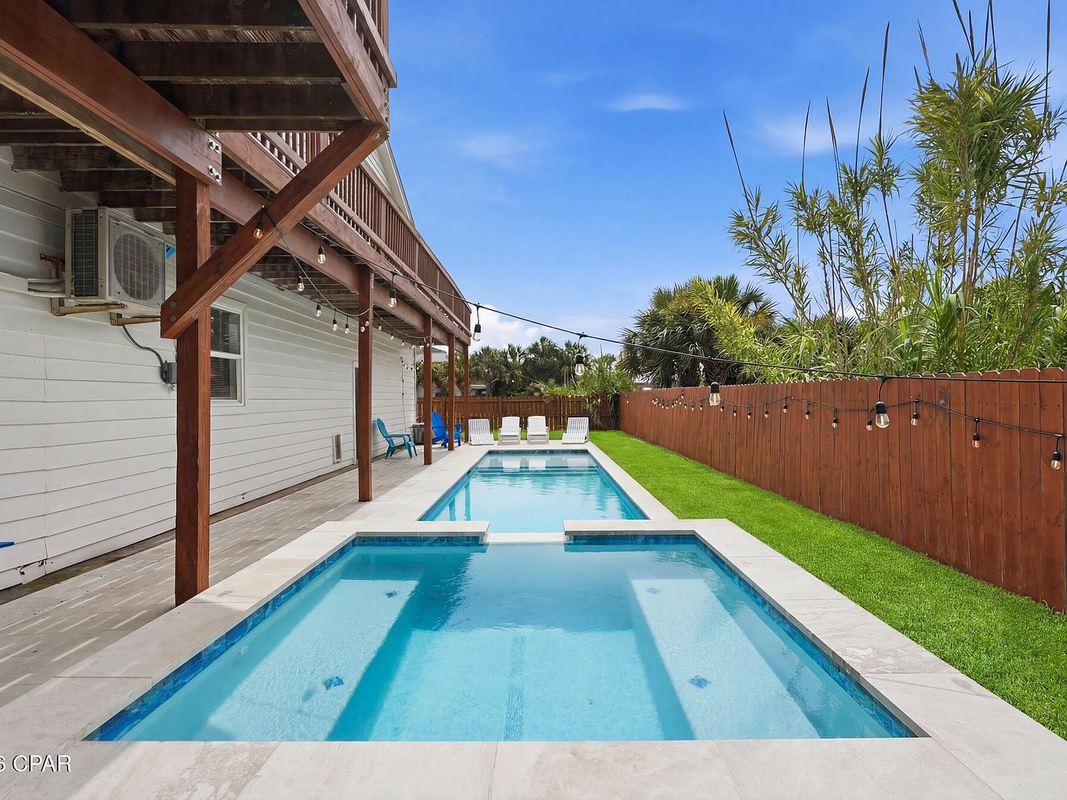 The heated lap pool and raised spa on a travertine deck at 1205 Via De Luna Dr, with string lights, a green turf strip, and a wood privacy fence