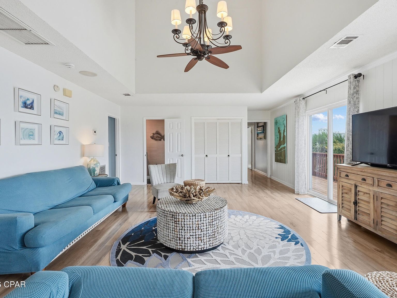 The great room at 1205 Via De Luna Dr with a vaulted ceiling, an iron-and-fan chandelier, blue sofas, and sliding glass doors to the deck