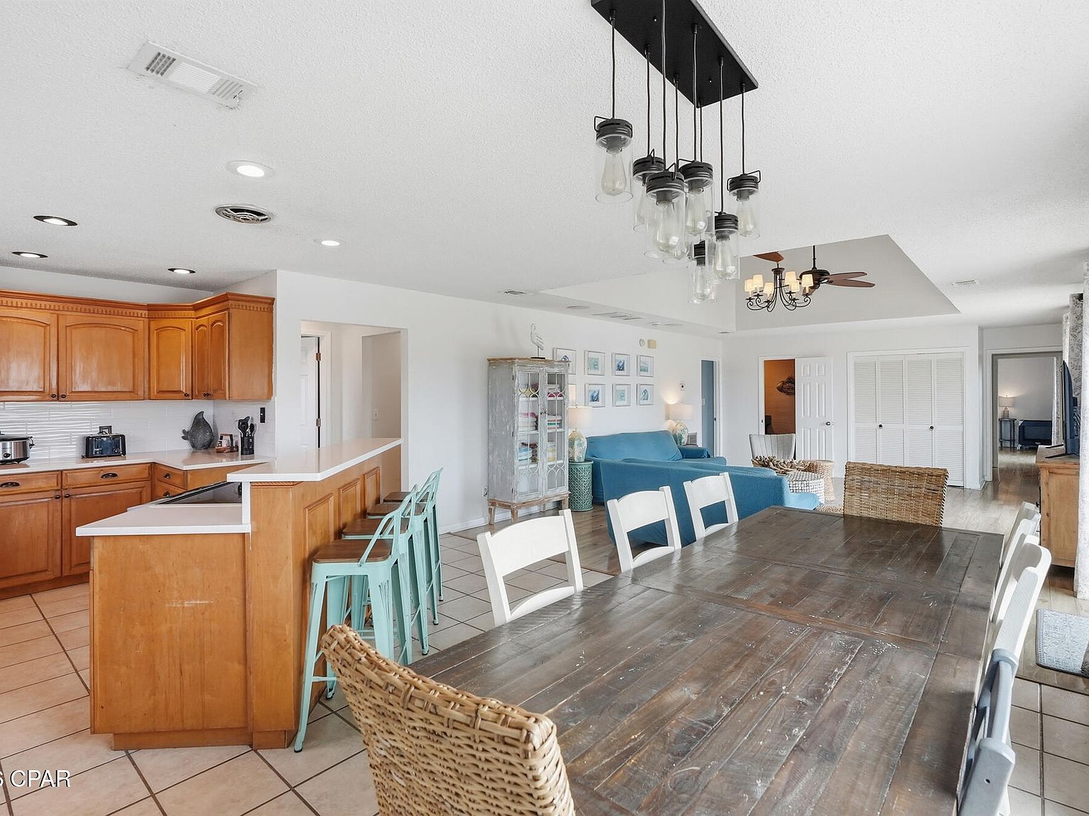 Open kitchen and dining area with wood cabinetry, a white quartz peninsula, turquoise barstools, a reclaimed-wood table, and a capiz-shell pendant