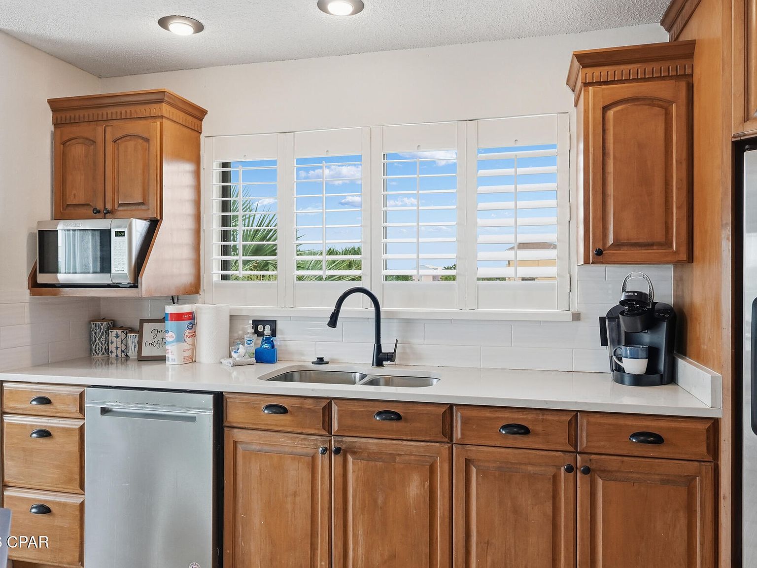 Kitchen detail at 1205 Via De Luna Dr: wood cabinets, quartz counters, a stainless dishwasher, and plantation-shuttered windows over the sink