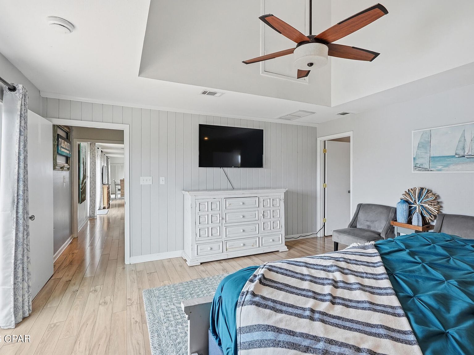 Primary bedroom with a tray ceiling, a gray shiplap accent wall, a wood-blade ceiling fan, light wood floors, and teal bedding