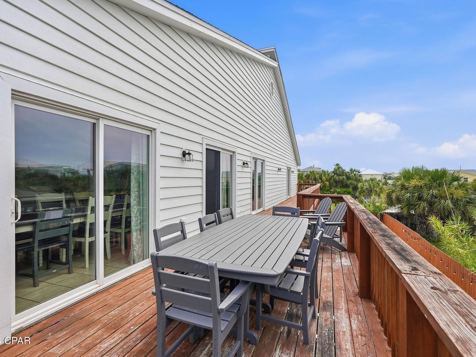 Upper sun deck with a long outdoor dining table and Adirondack chairs, looking out over treetops toward the water